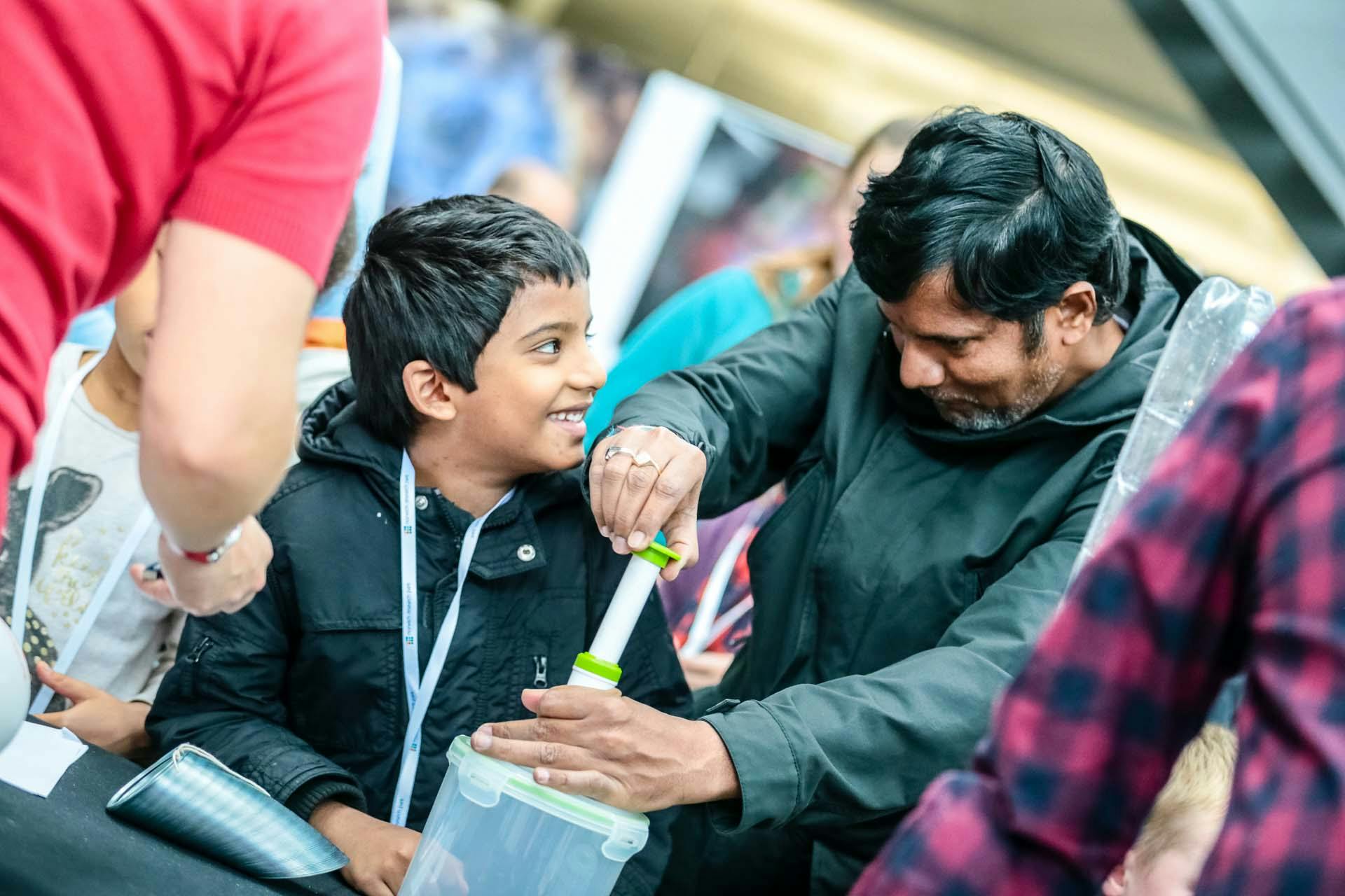 A boy looks at his father smiling while he does a science experiment