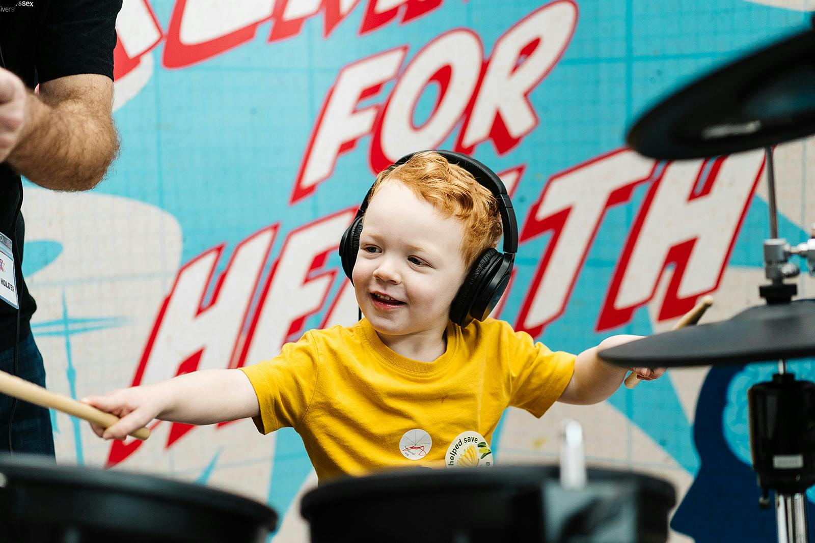 A young child playing the drums, wearing headphones