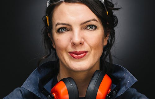 A woman with dark hair wears a pair of ear defenders and goggles