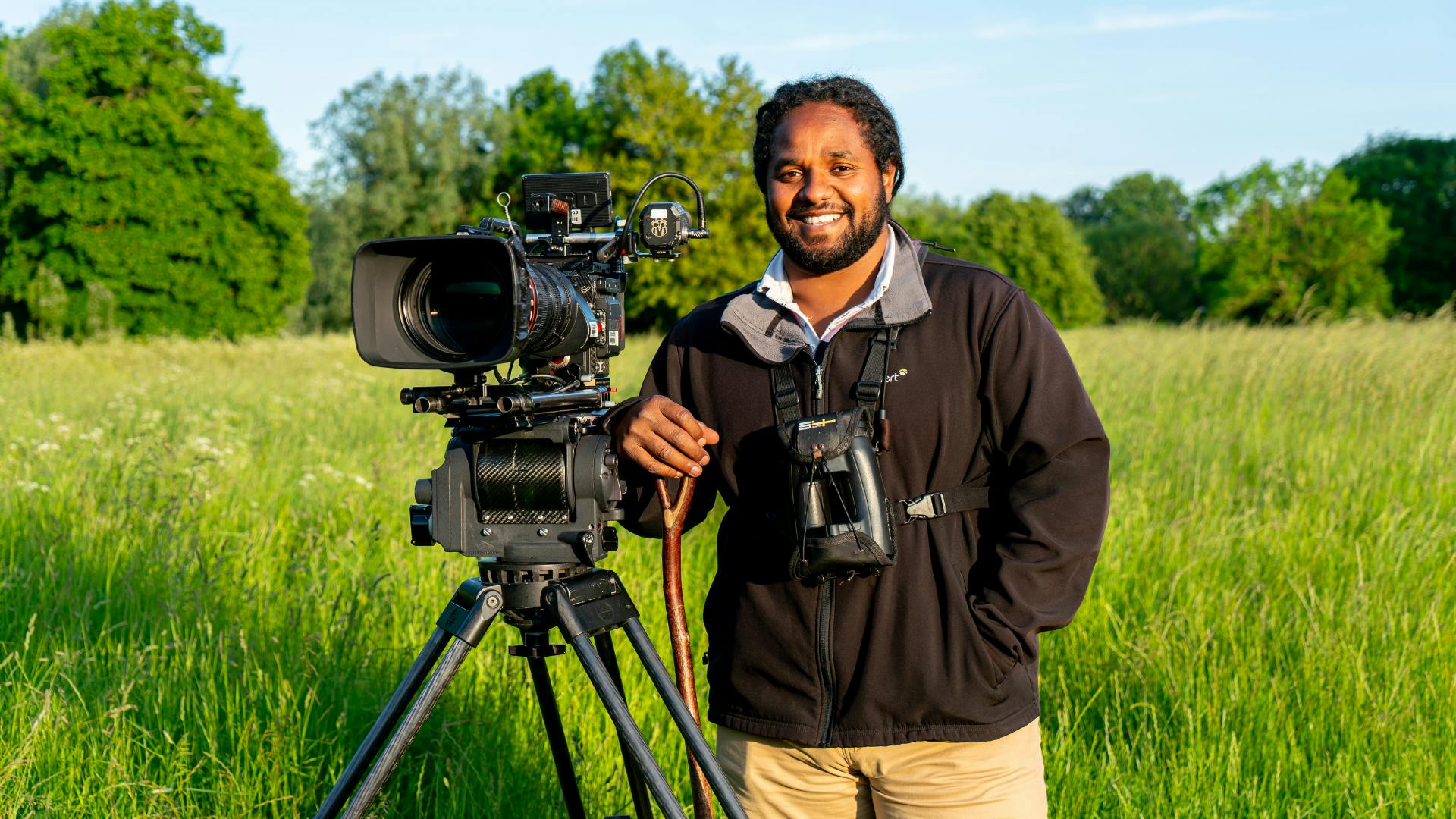 A man with a pair of binoculars stands next to a large TV camera