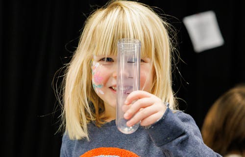 Little girl with face paint on her cheek holds up a plastic test tube