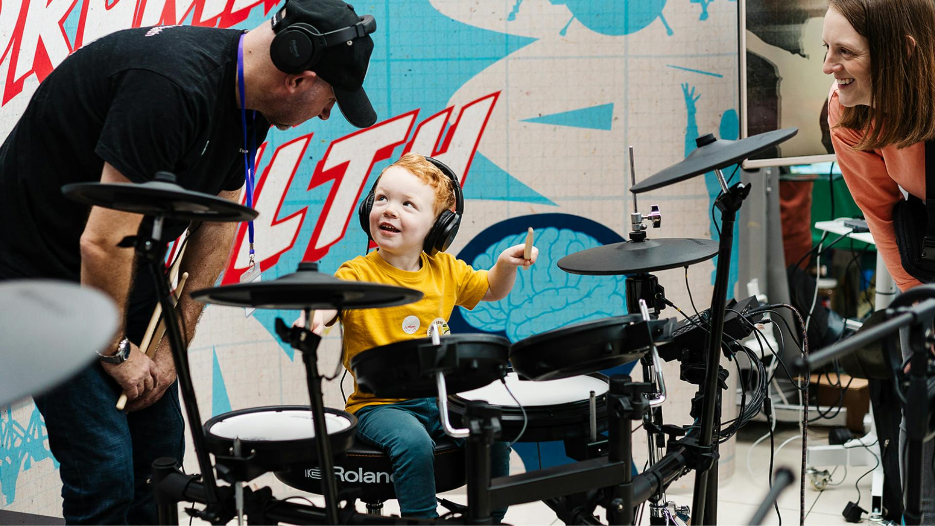 A young child playing the drums, wearing headphones