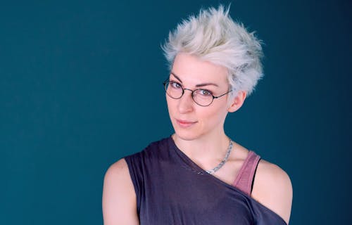 Iszi Lawrence, wearing dark top and glasses, against a blue background. Image credit Steve Cross