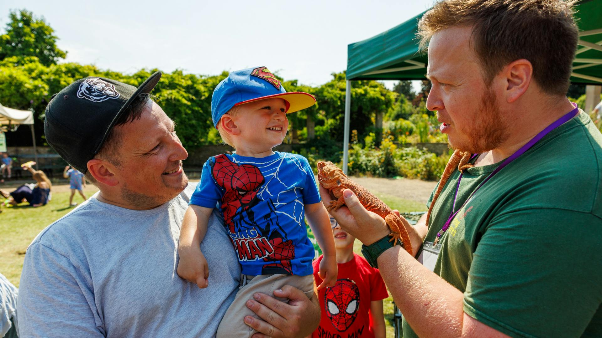 A small child with parent smiles as they meet a bearded dragon at Bugs and Beasts 2024