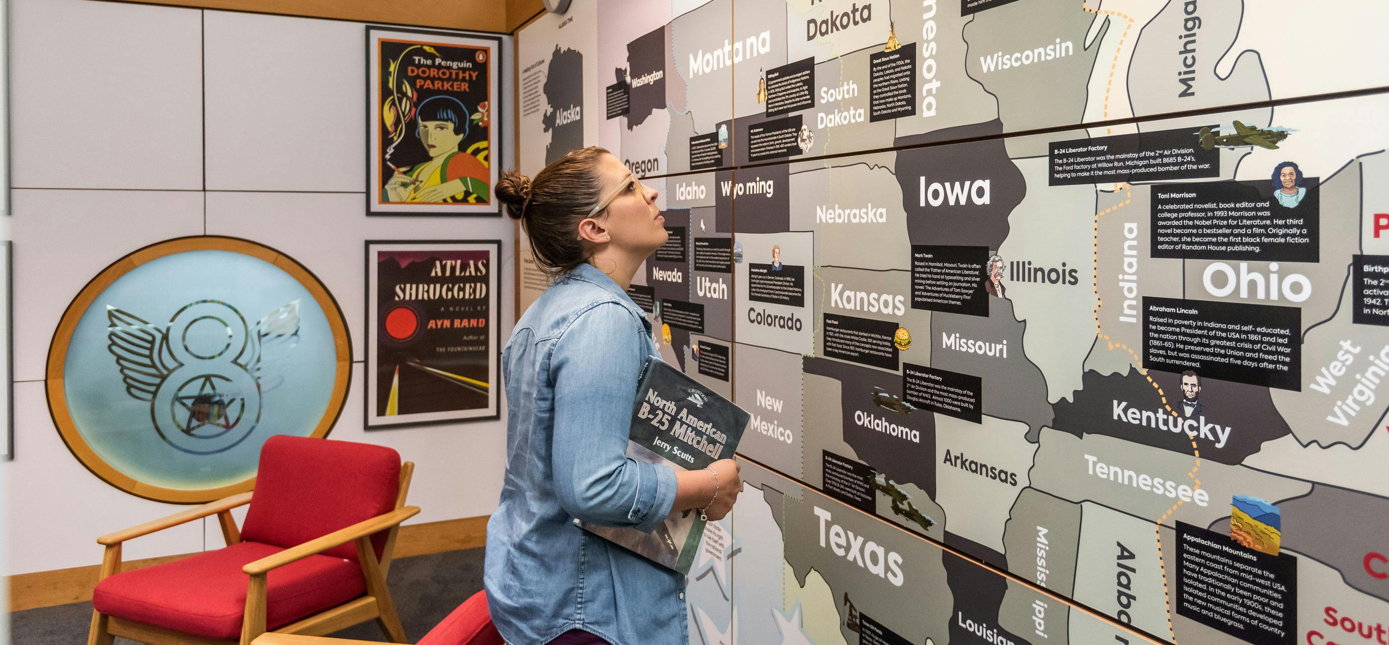 A woman looks at a map of the USA, holding a book.