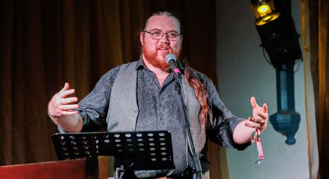 Poet Benjamin Macpherson speaking on stage.
