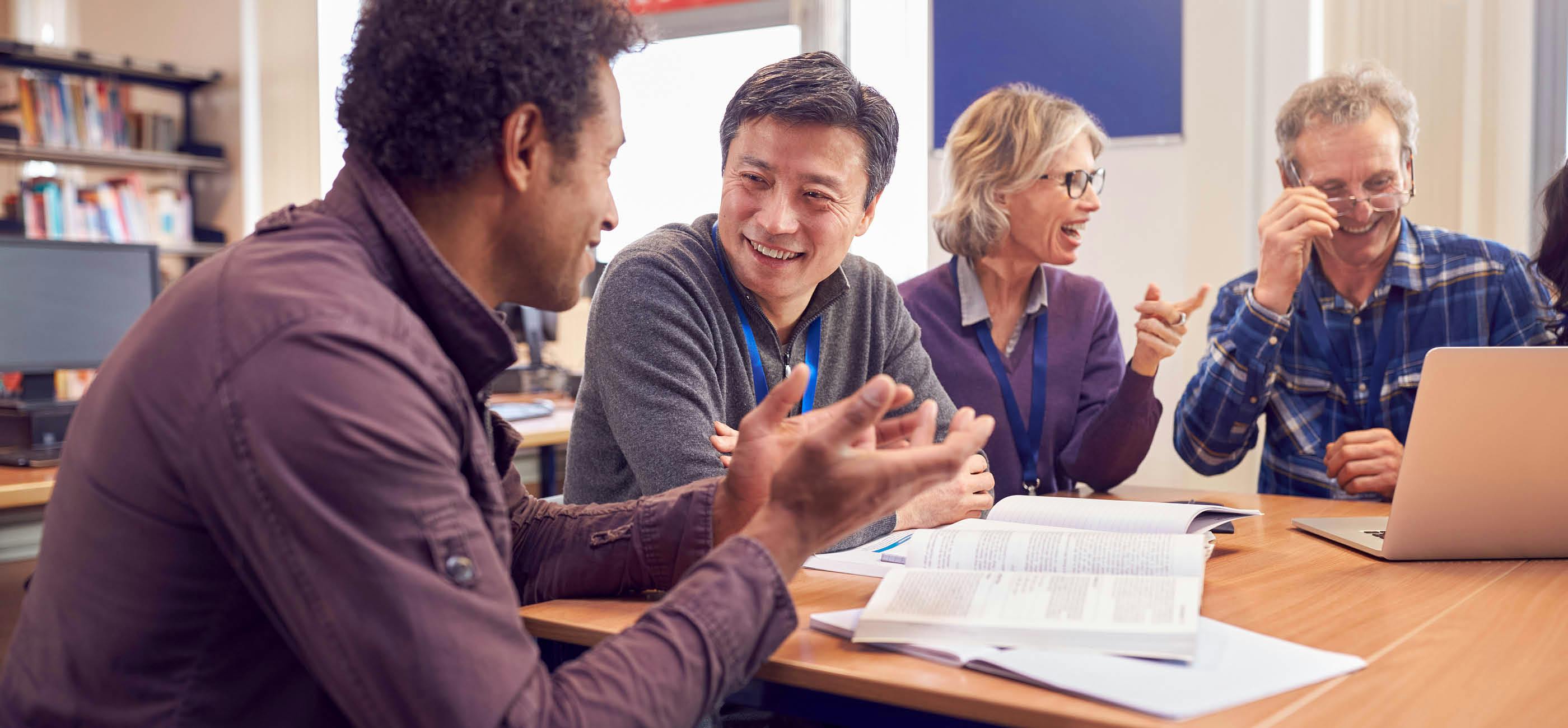 A group smiling and discussing over a laptop and books