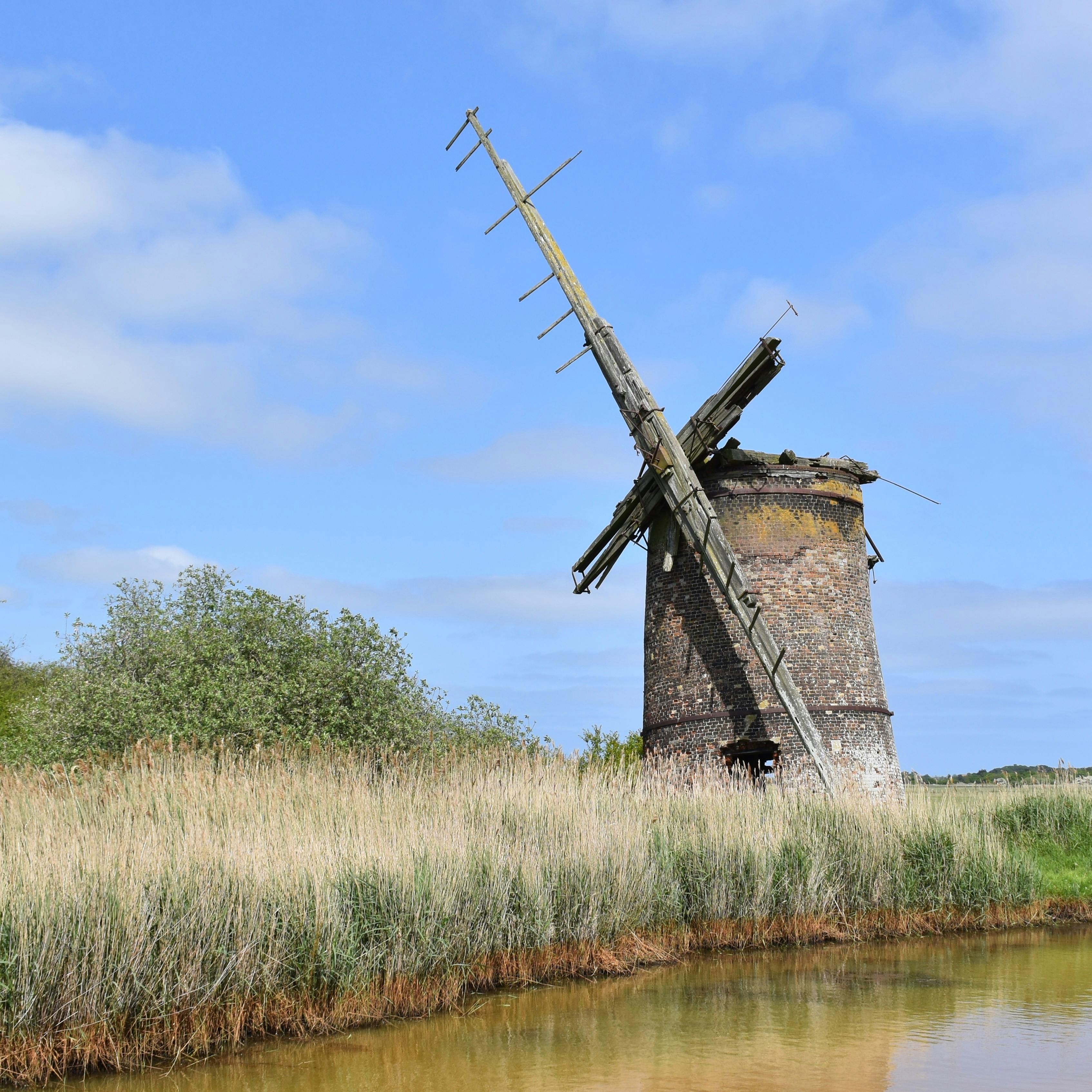 An old, abandoned windmill with broken sails next to a Norfolk broad.