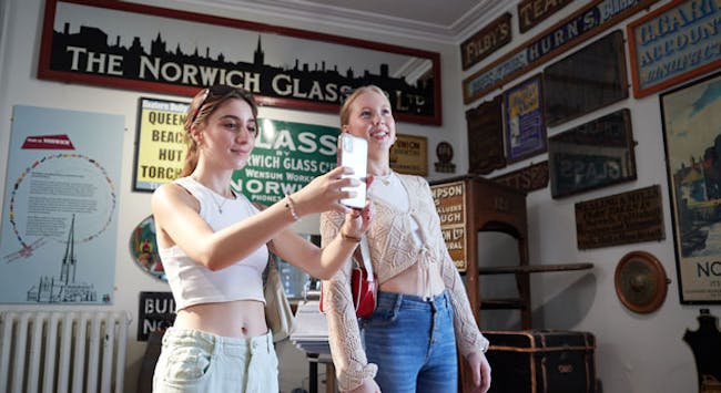 Two young women take a picture on there phone in a museum full of old shop signs