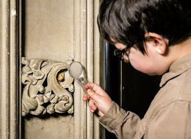 A child looks at a stone decoration with a magnifying glass.