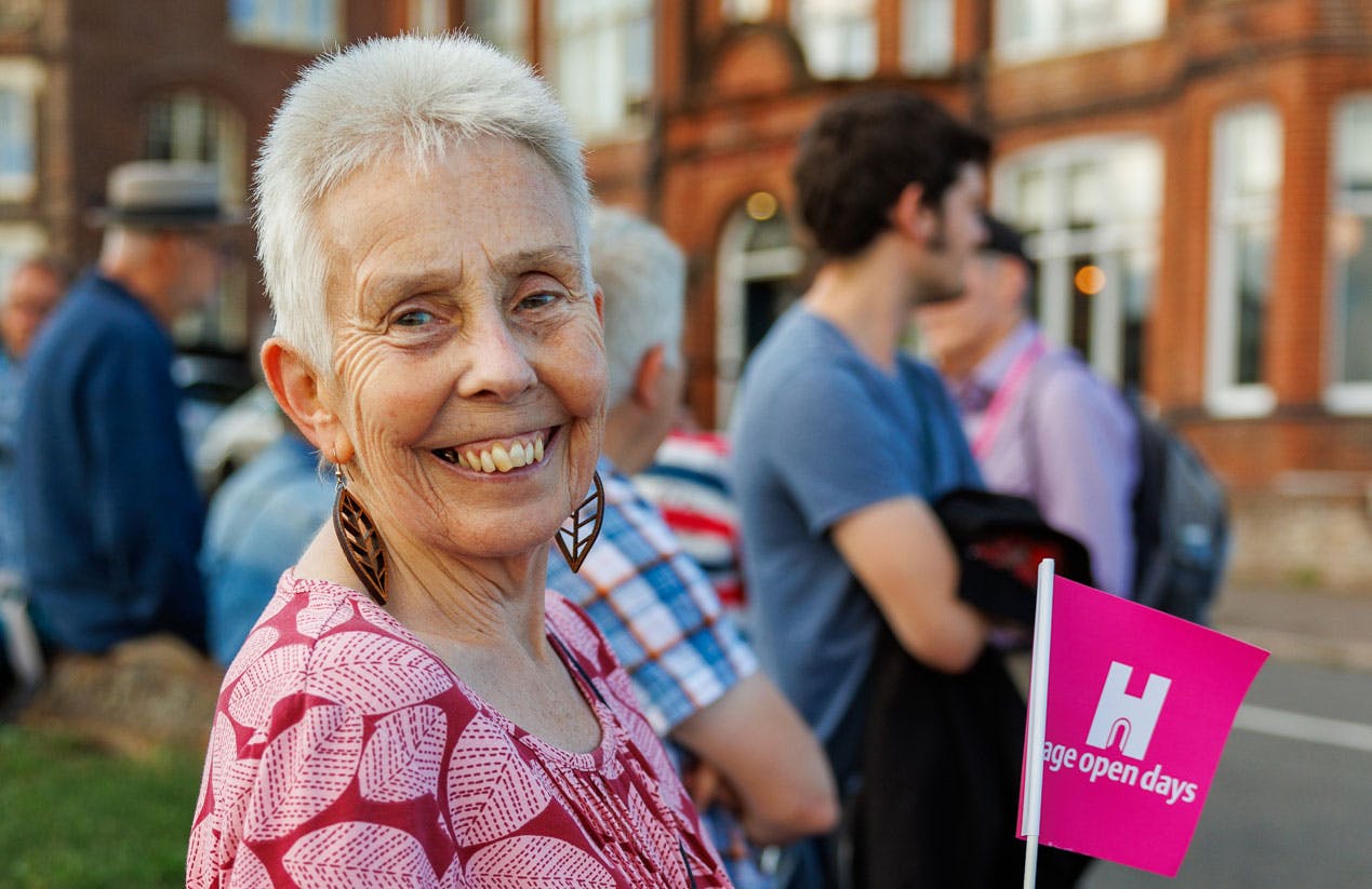 A women on a walking tour smiles at the camera holding a pink Heritage Open Days flag.