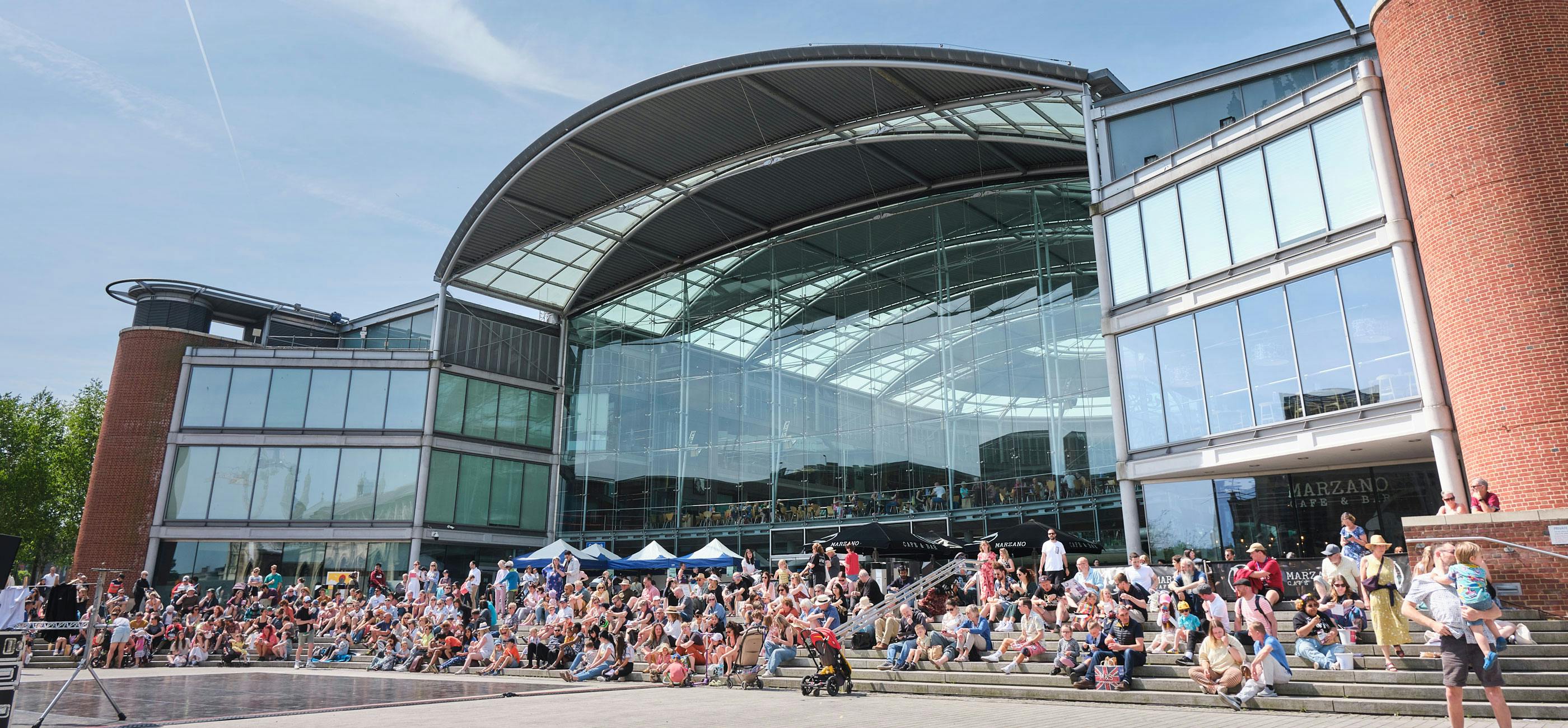 A crowd of people outside The Forum in the sun