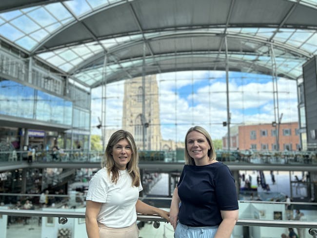 Two women stood in a glass building, smiling