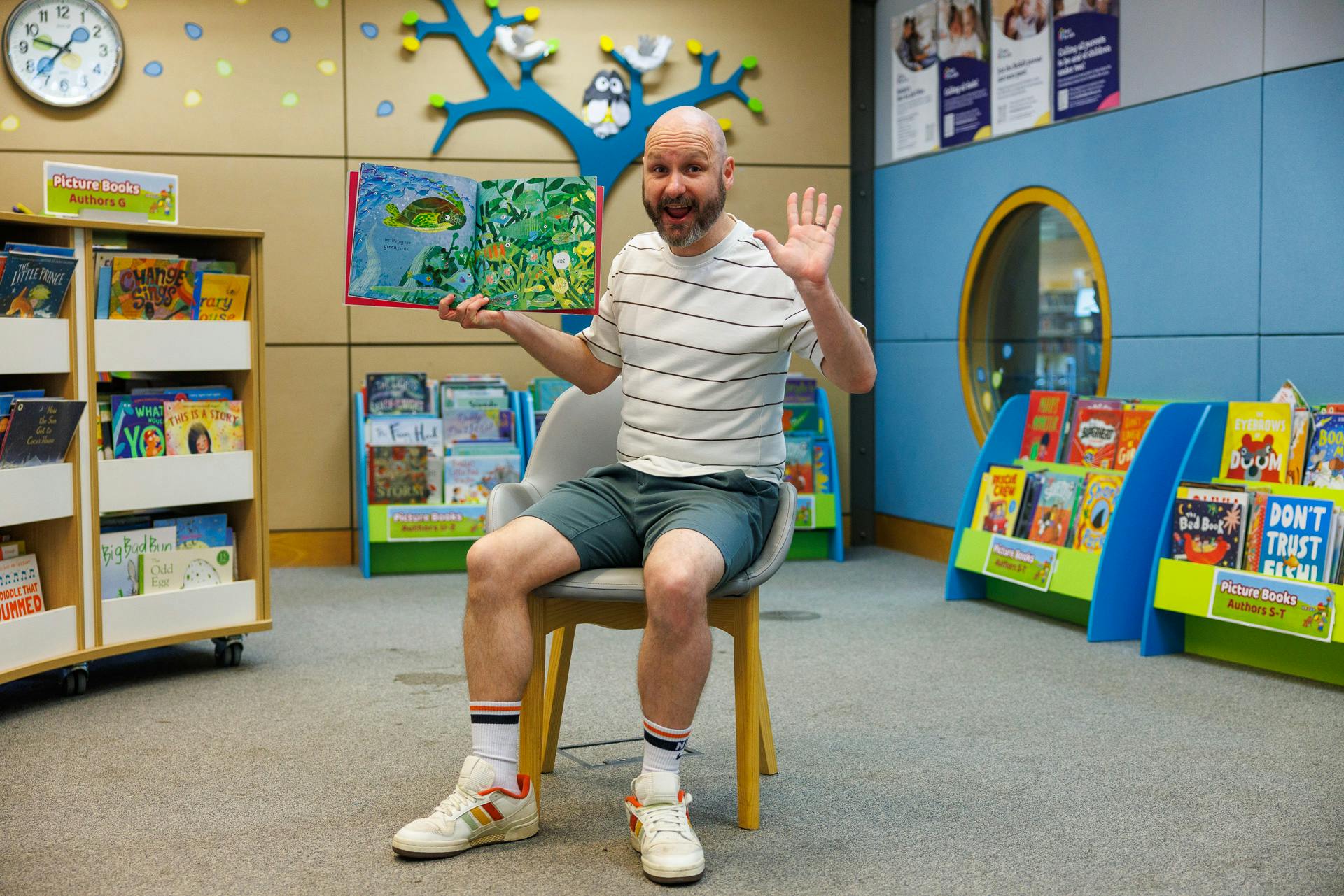 Adam from The Millennium Library sitting in a chair with a colourful picture book