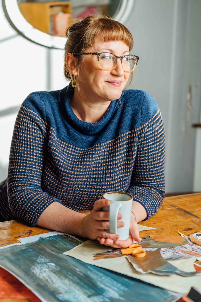 Kate Read, a young white woman with glasses sitting at a table holding a coffee cup