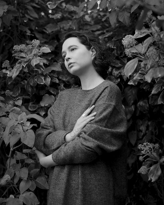 A black and white image of AK Blakemore standing sideways on in front of foliage.