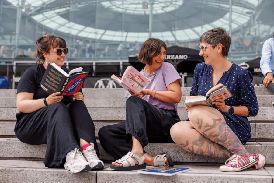 A picture of three women sitting on the steps of The Forum, holding books and talking and smiling.