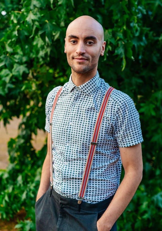 A head and shoulders shot of Tom, a young black man wearing braces, standing in front of a shrub