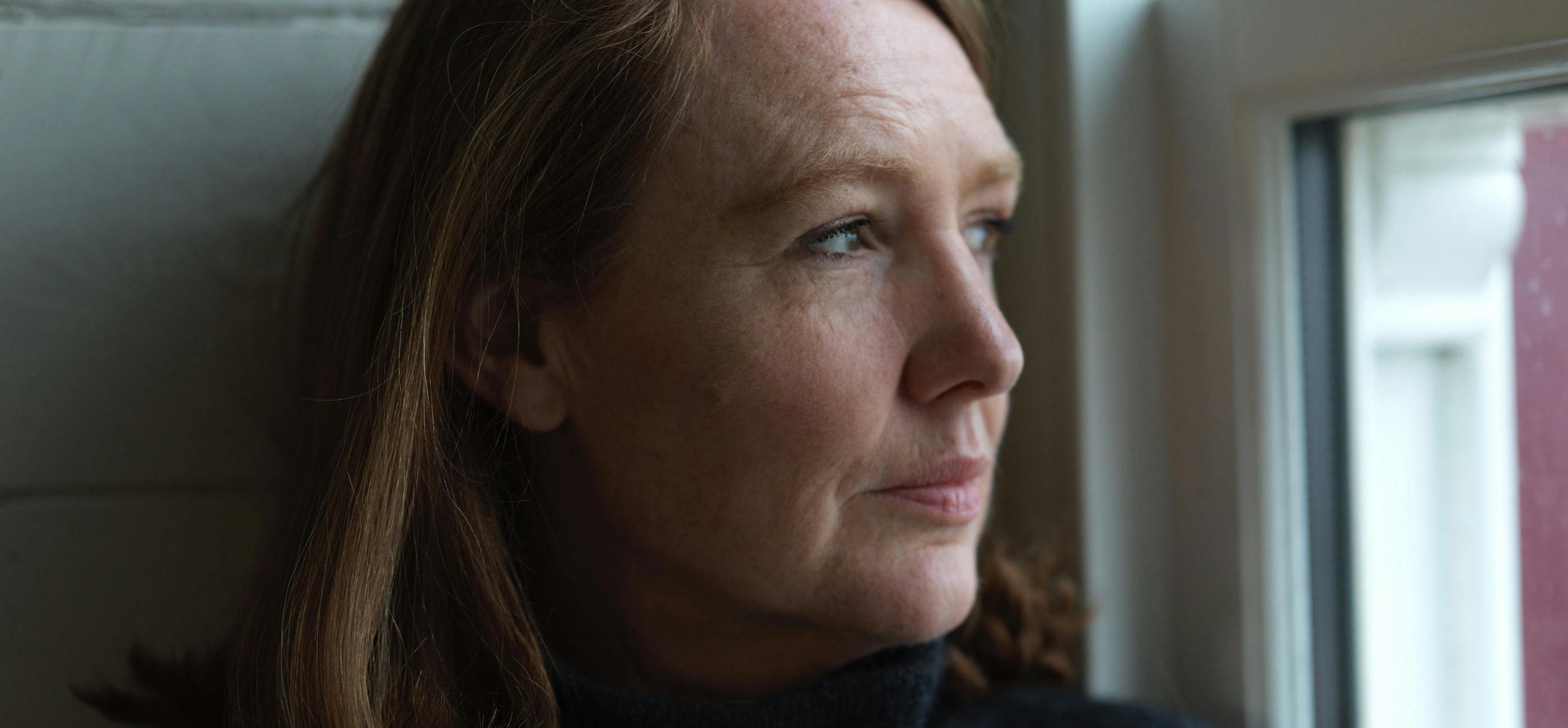 Photograph of woman with bobbed brown hair looking out of the window