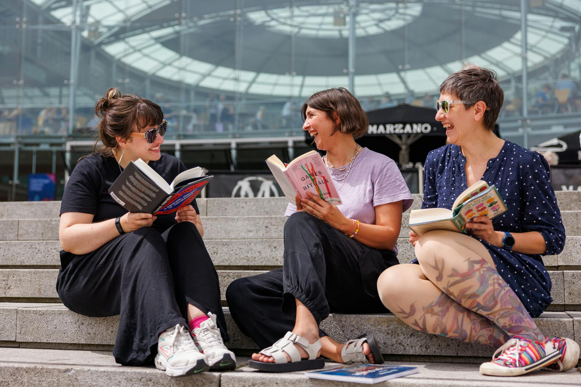 three women sitting on the steps of The Forum reading books and laughing