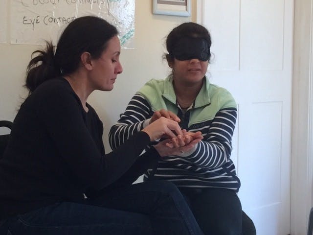 A woman teaching tactile signing to someone wearing a blindfold.
