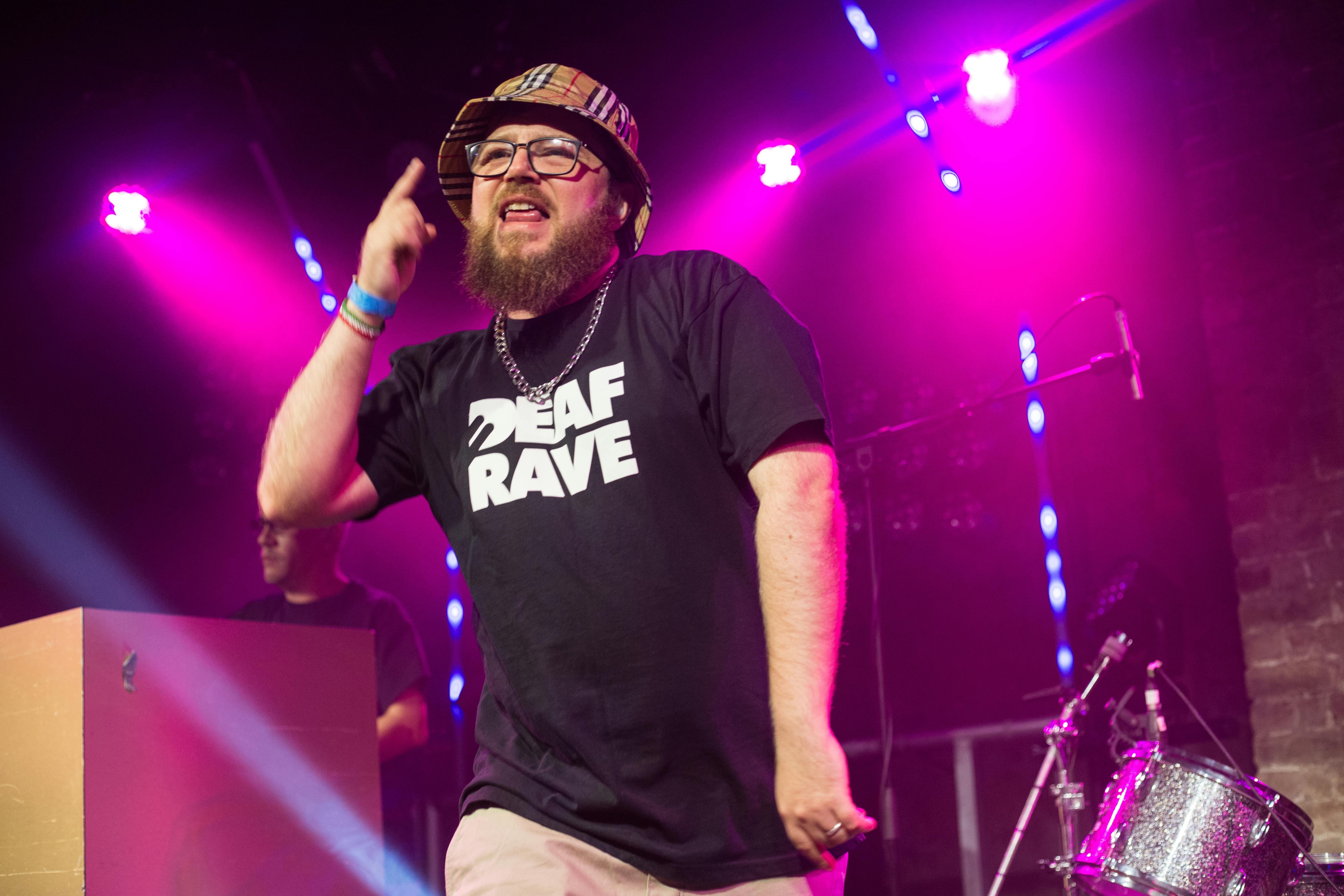A bearded man with glasses and a bucket hat performing on stage.