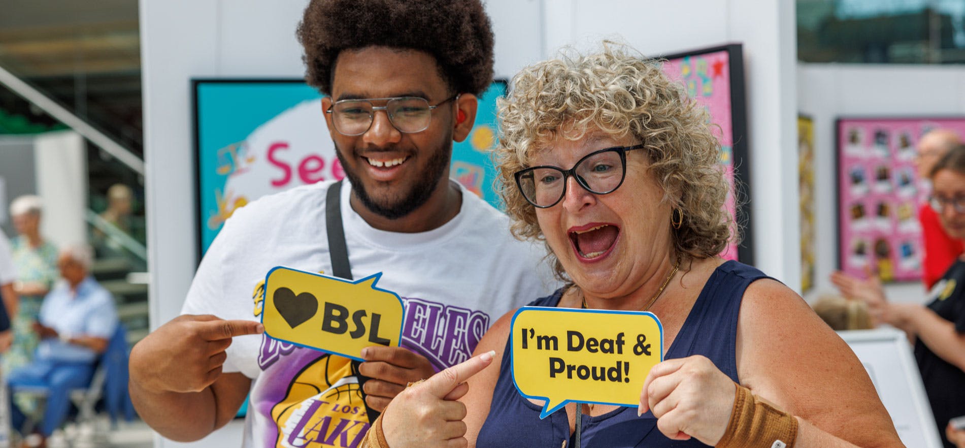 A man and women hold up signs saying I'm Deaf and Proud