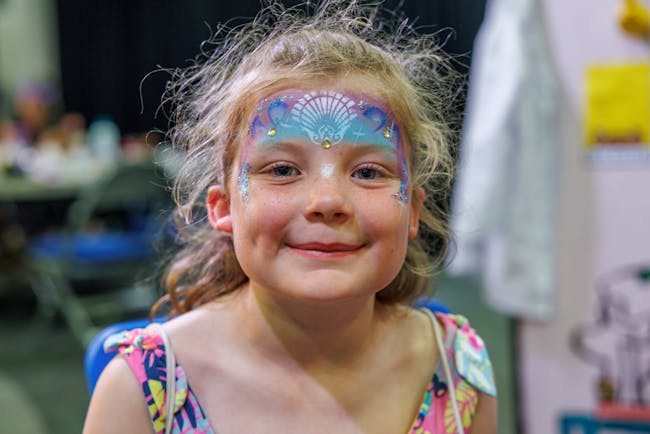 A young girls with sea themed face-paint smiling at the camera