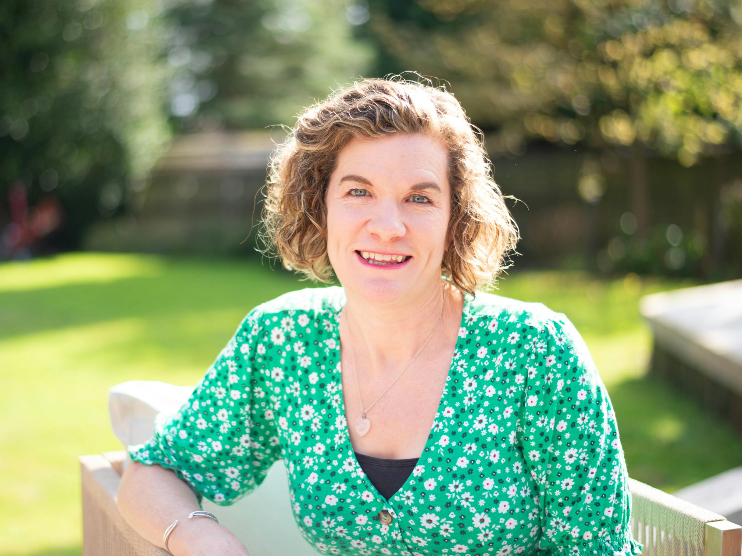 Photograph of Nicci Rossini sitting in a garden smiling.