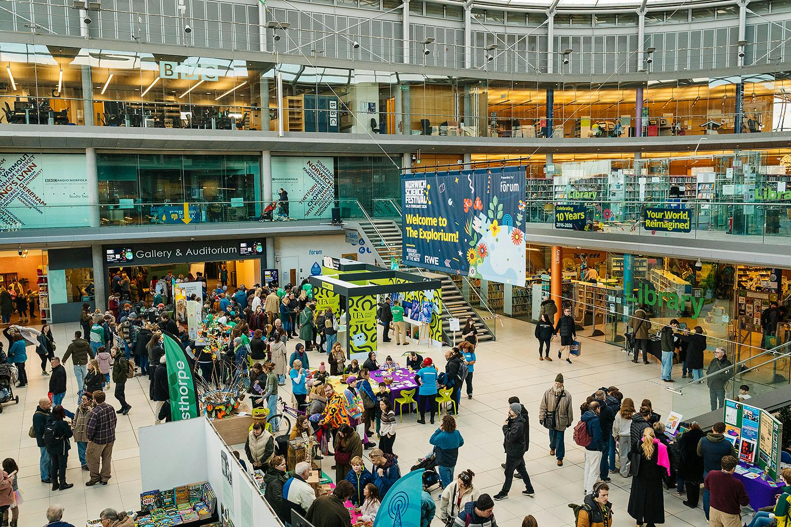 A bustling festival with colourful activity stalls and lots of visitors at The Forum in Norwich.