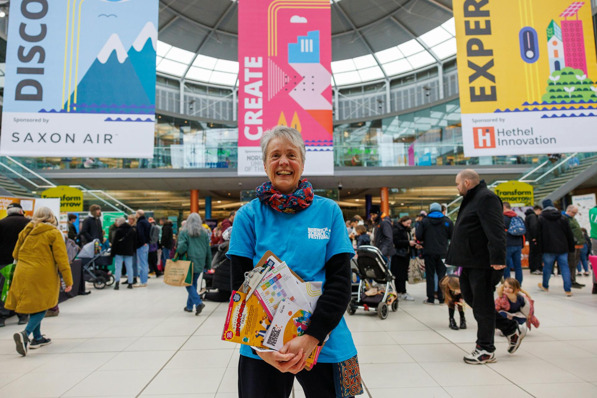 A volunteer in a bright blue tshirt smiles in the centre of The Explorium