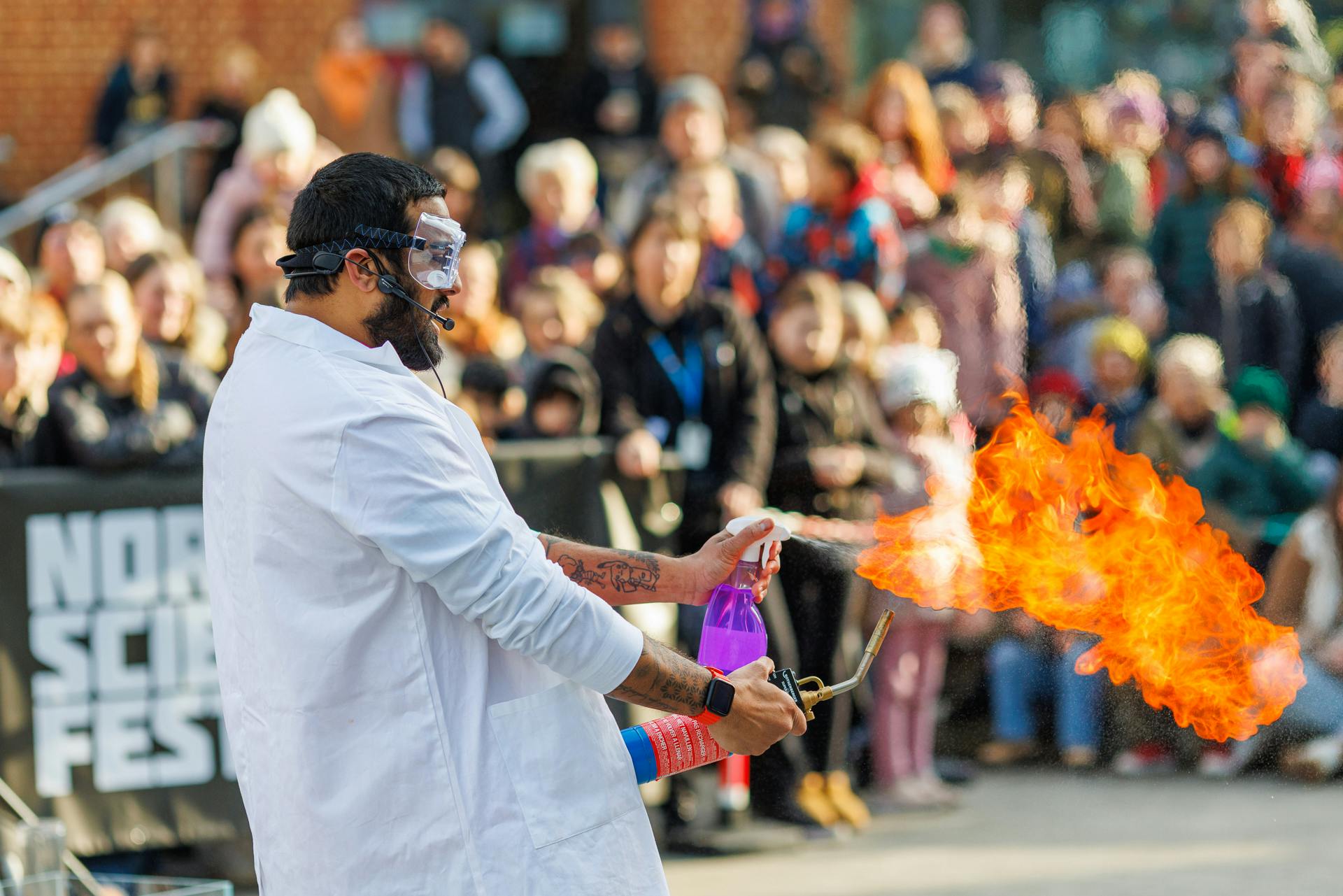 A performer showcases a fire demonstration with a large crowd at NSF25