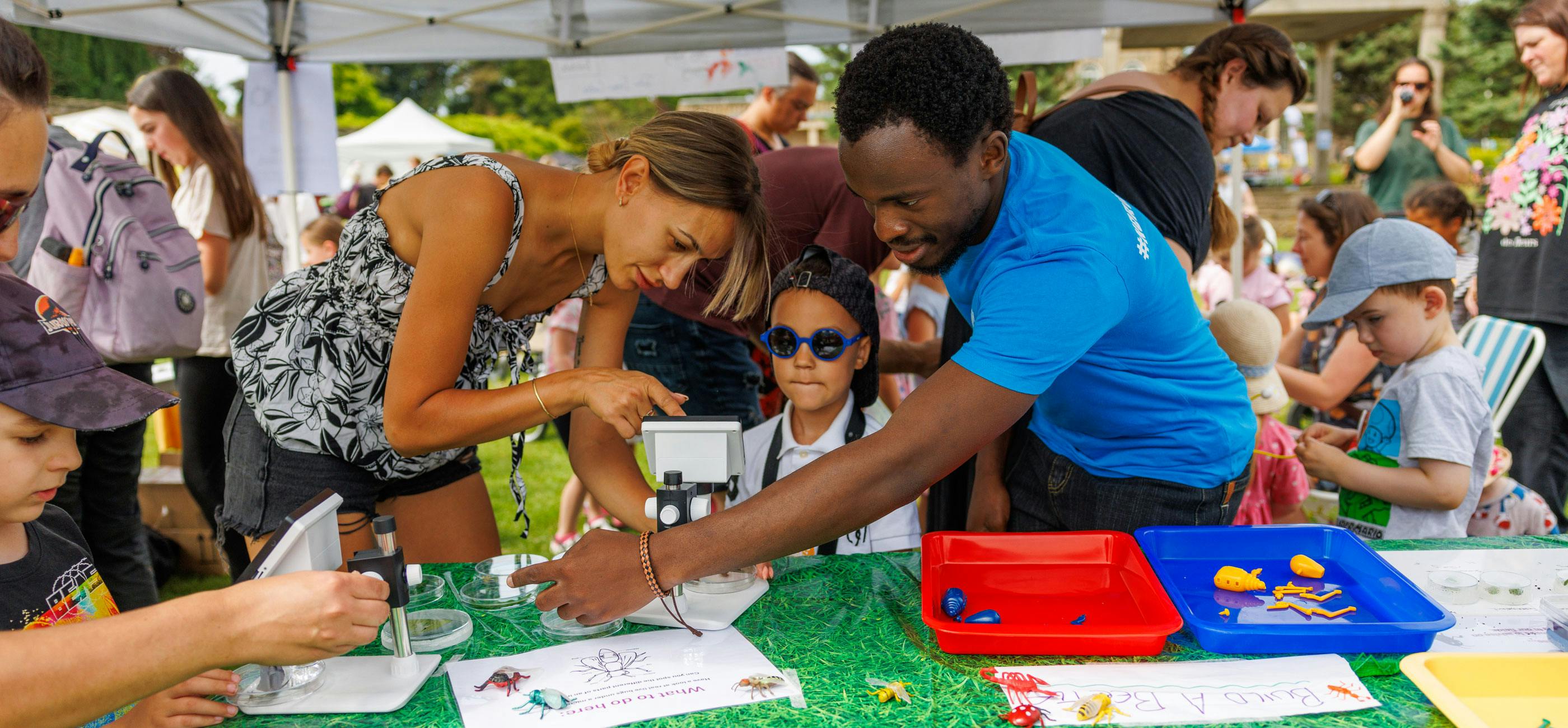 A woman, child and member of the Norwich Science Festival team taking part in an activity looking at bugs with a microscope.