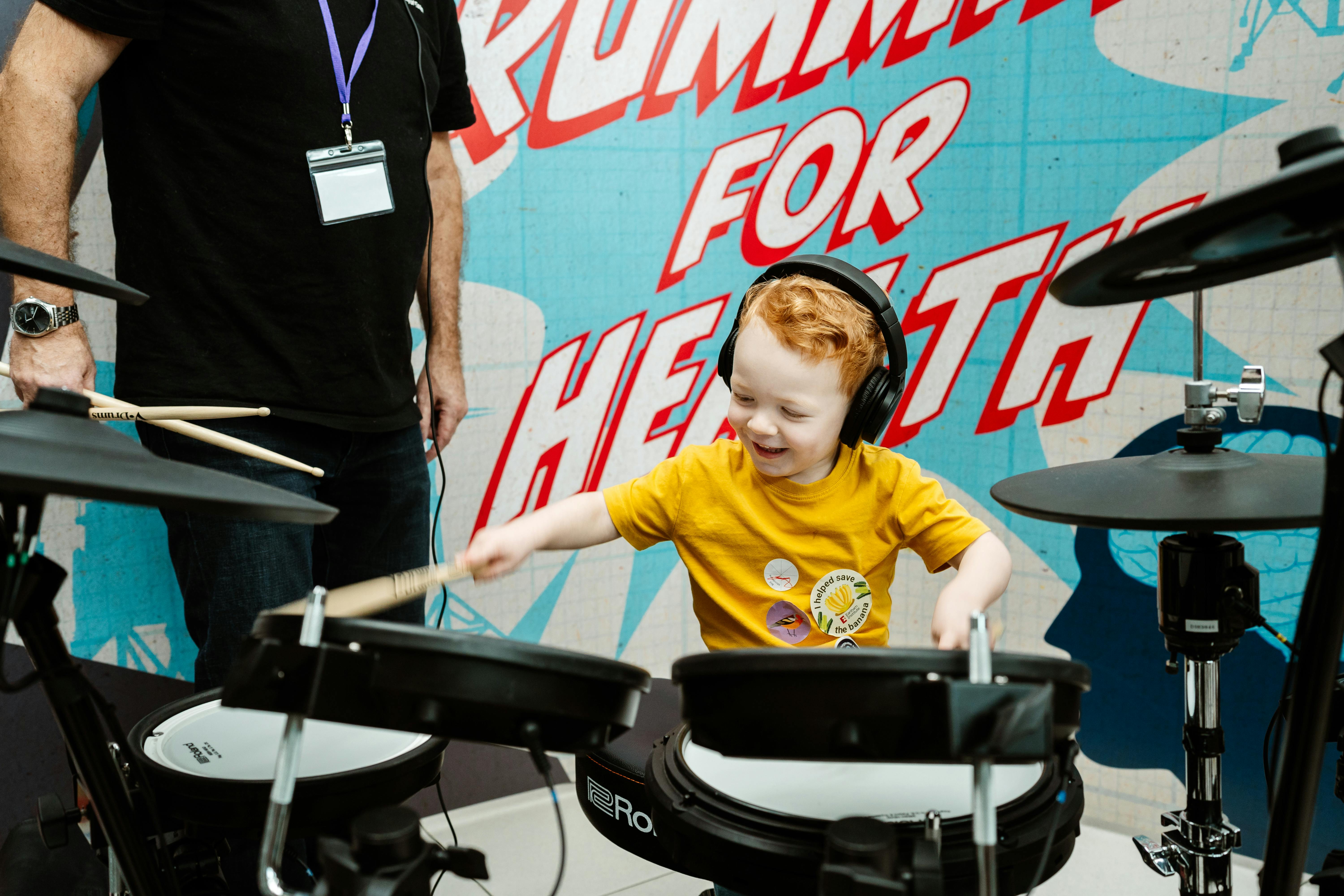 A young child playing the drums, wearing headphones