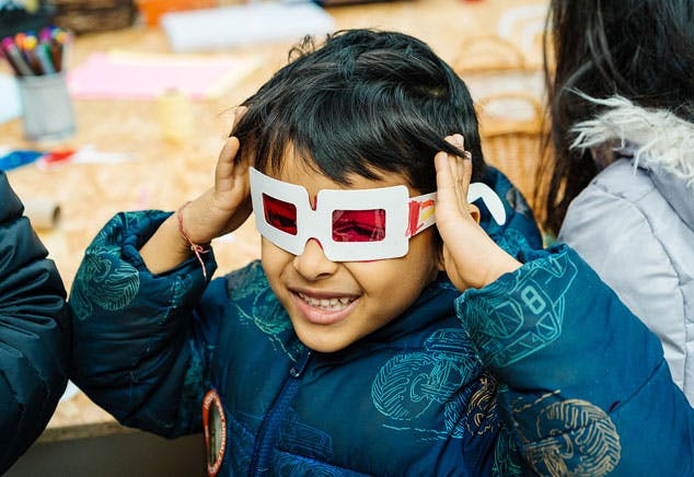 A child smiles wearing his hand made red glasses