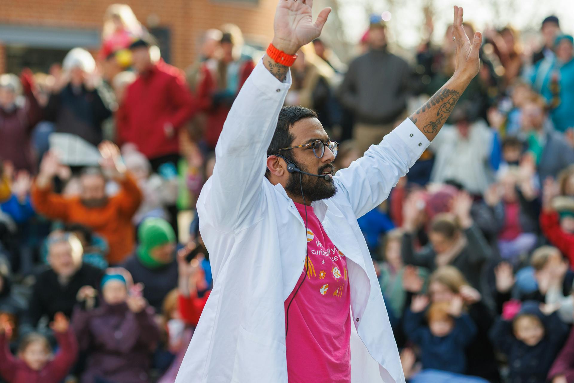 Nikhil Mistry in a white lab coat holding his hands in the air speaking to a crowd.