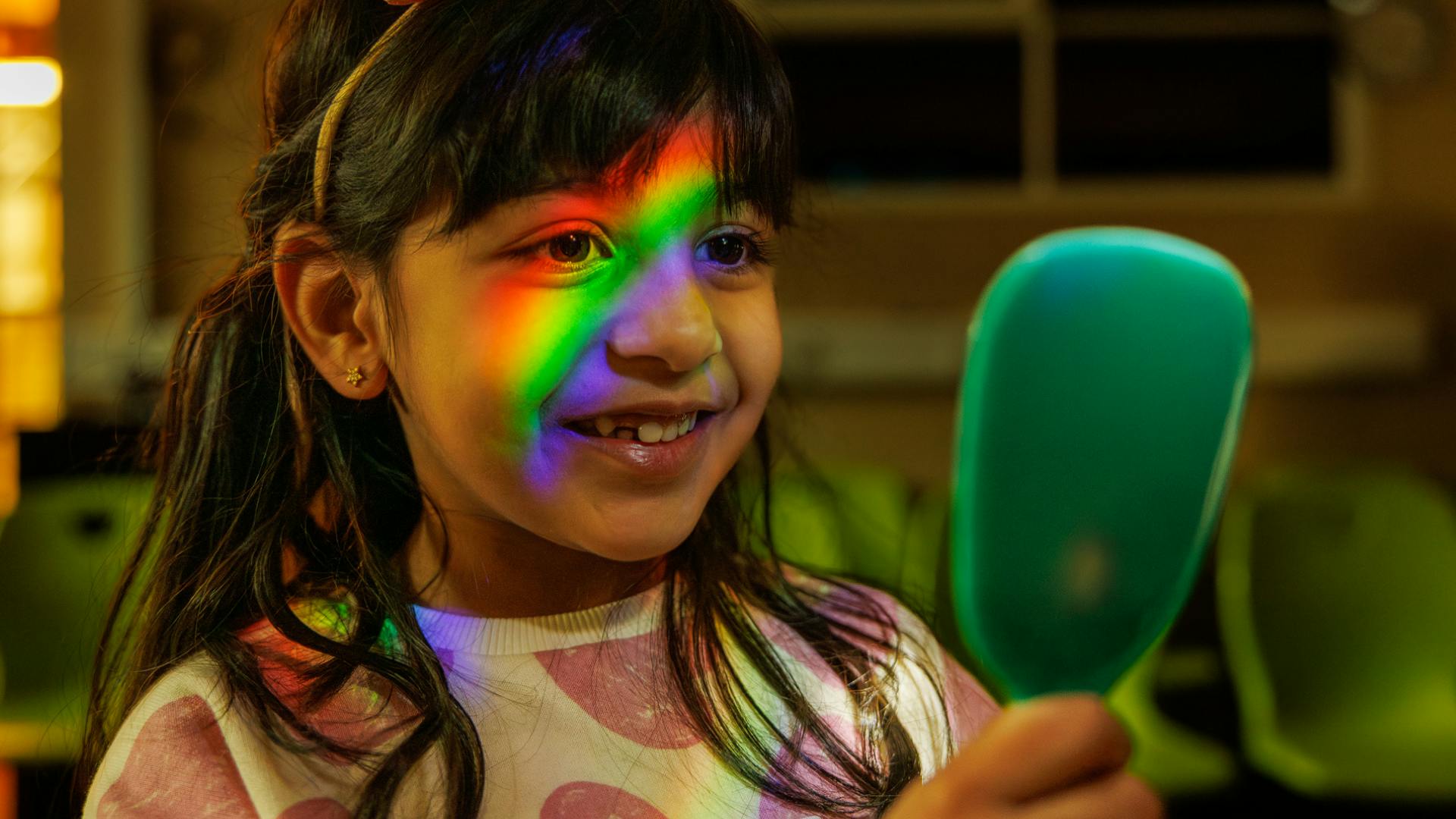 A child smiles into a mirror as a rainbow of light is shone onto her face.