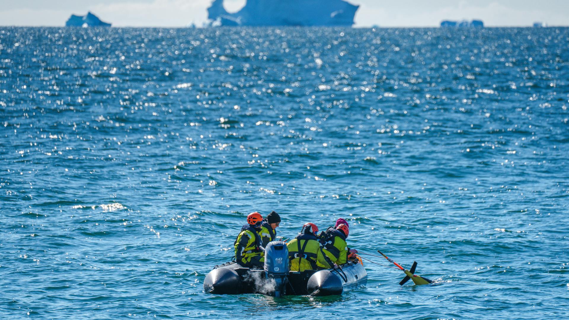 web-when-icebergs-collapse-2.png Five people at sea in a small inflatable boat.