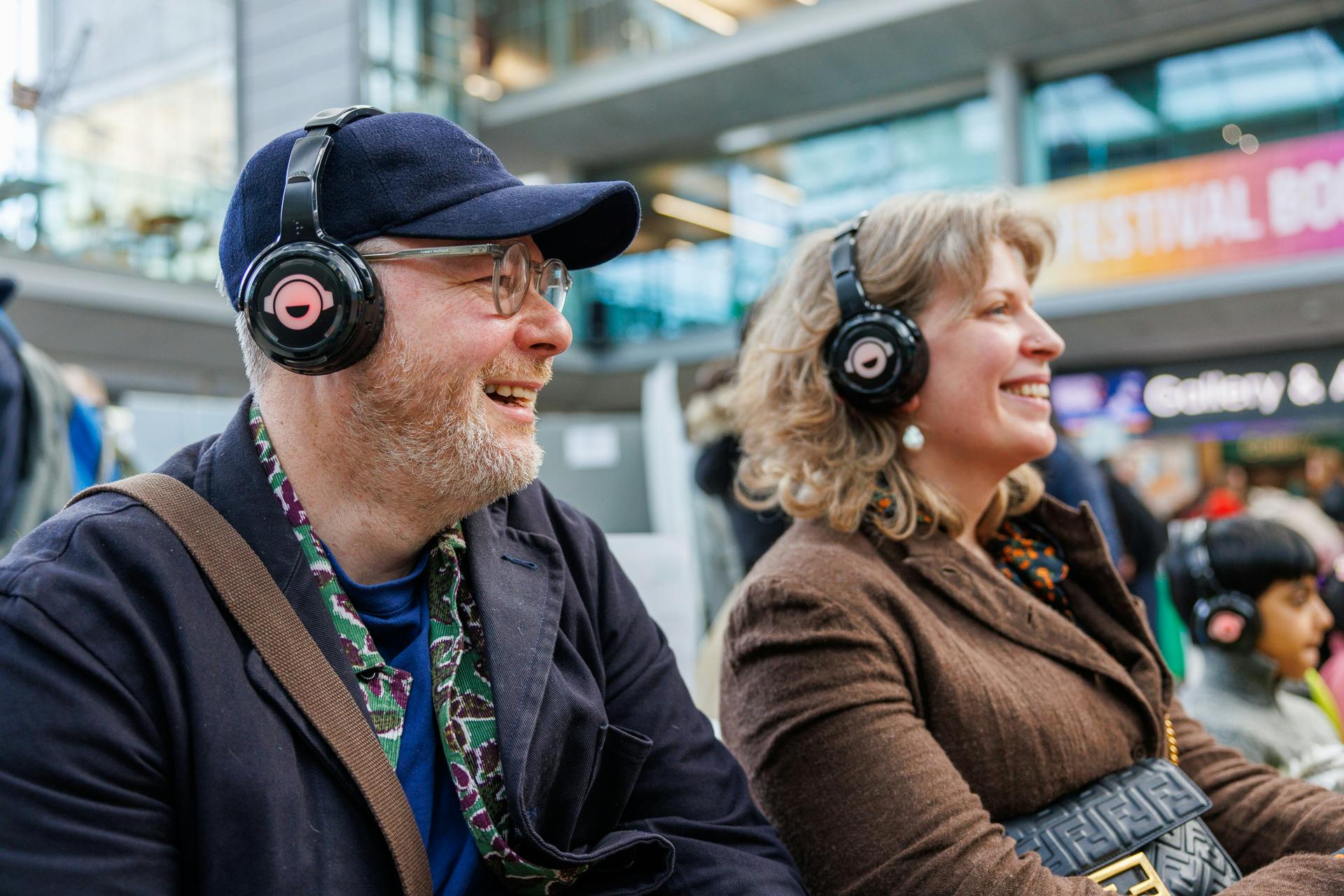 Two smiling visitors wear headphones inside The Explorium.