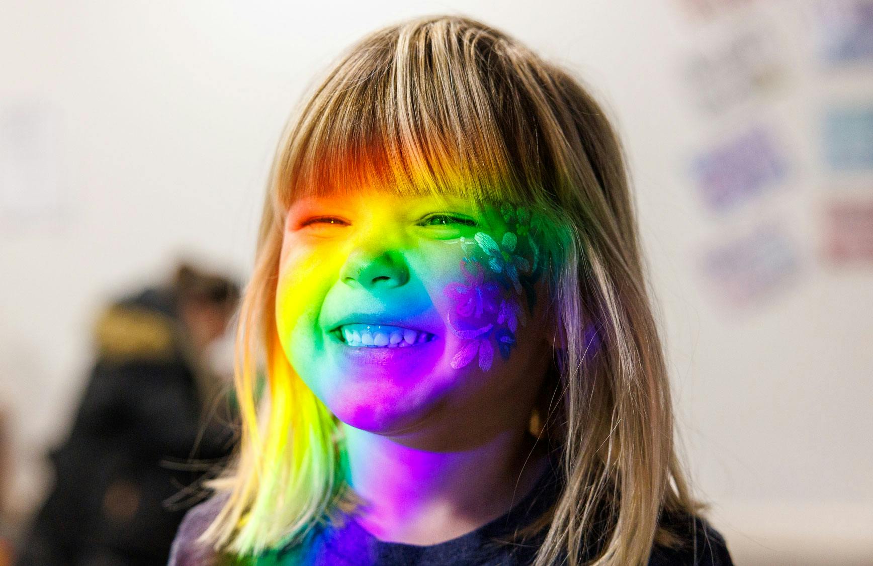 A girl with smiles with a rainbow of light across her face.