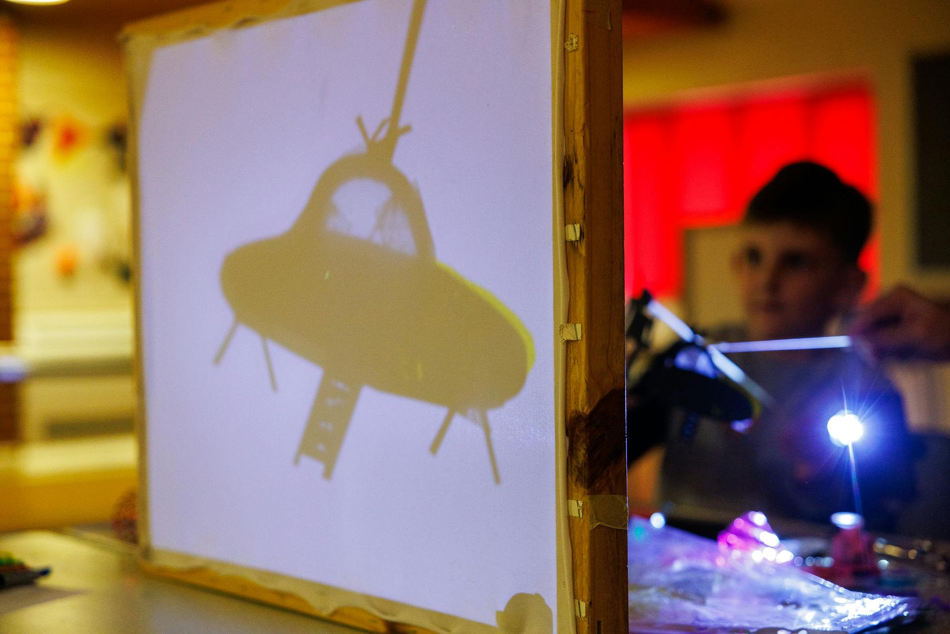 A spaceship shadow puppet is held up in front of a torch.