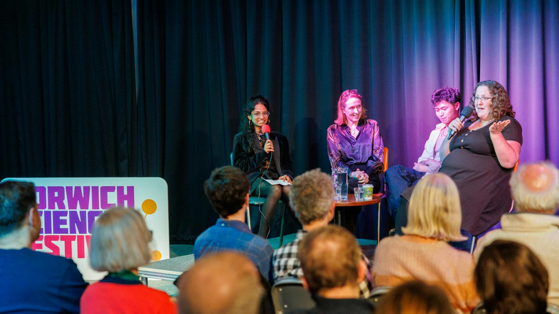 Four people talking on stage in front of an audience.