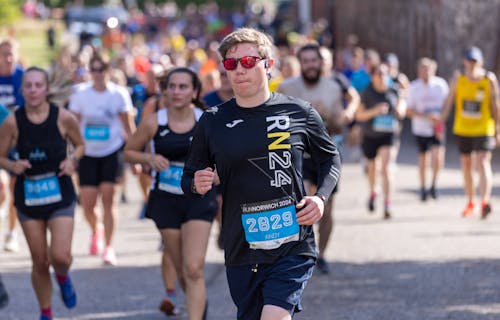 Man dressed in black t-shirt and shorts wearing red sunglasses concentrating while running.