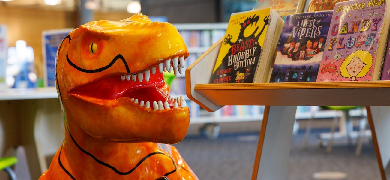 Orange model dinosaur next to a shelf of books