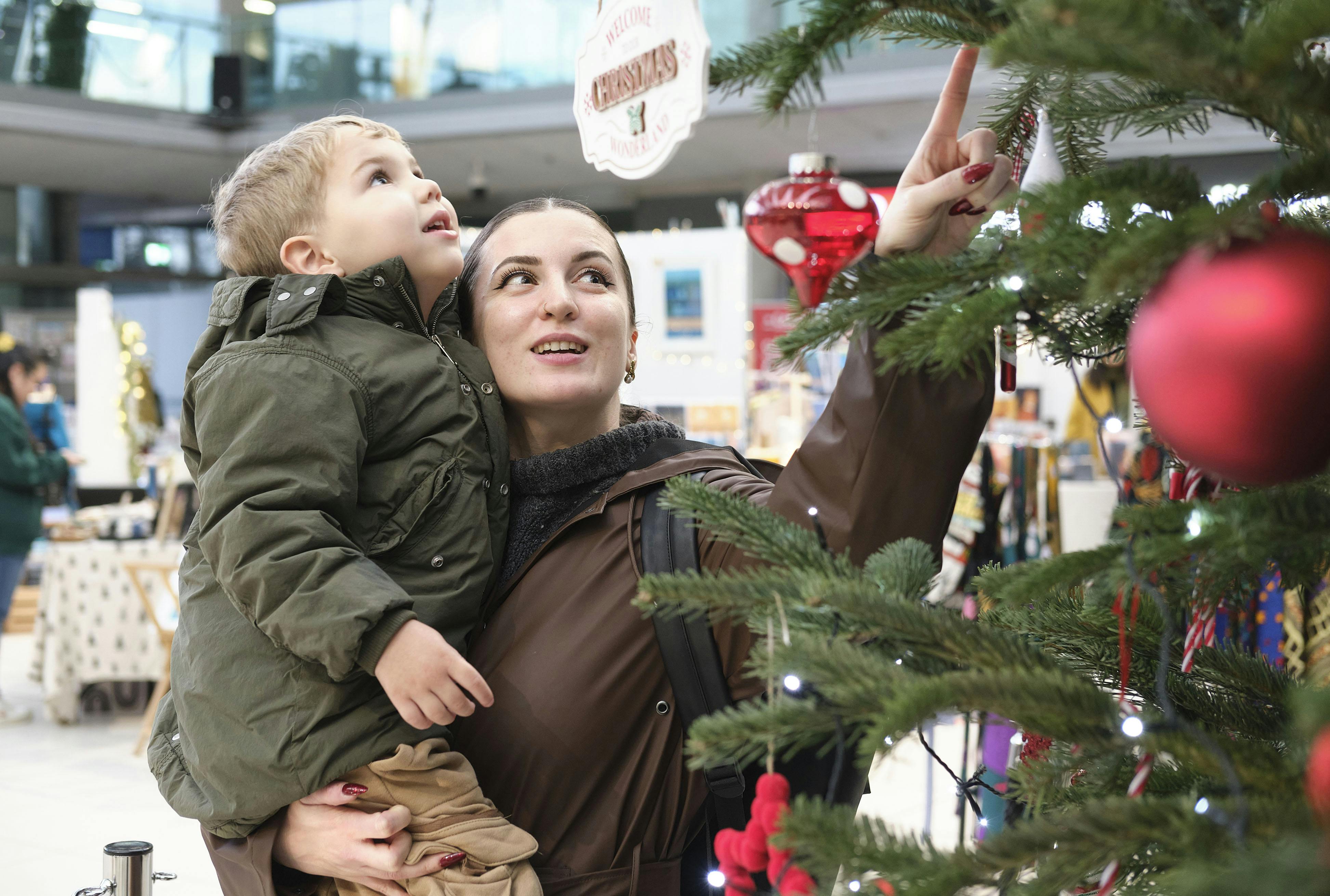 A woman holding a toddler and pointing up at a decoration on a Christmas tree