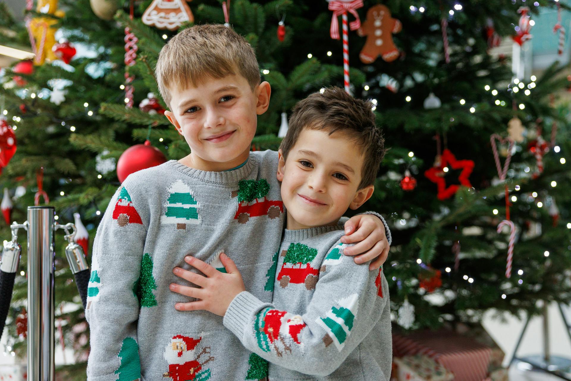 Two boys in festive jumpers, embracing in front of a Christmas tree